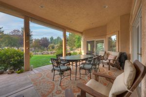 Spacious covered outdoor patio with dining table, seating area, decorative rug, and scenic garden views.