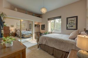 Bright master bedroom with vaulted ceiling, pendant light, mirrored closet doors, and garden window view.