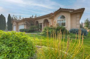 Mediterranean-style single-story home with arched windows, stucco exterior, and lush landscaping.