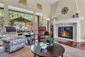Cozy living room with stone fireplace, vaulted ceilings, hardwood floors, and large windows with patio view.