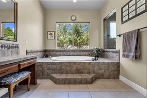 Luxurious master bathroom with tiled soaking tub, dual vanity, large window with tree views.