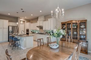 Open dining area with chandelier, wood table, and view into white kitchen with large island.