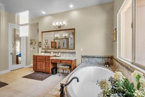 Master bathroom featuring soaking tub, dual vanity with mirrors, tile floors, and natural lighting.