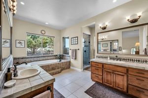 Spacious bathroom with dual vanity, soaking tub, tile floors, walk-in shower, and warm wood cabinets.