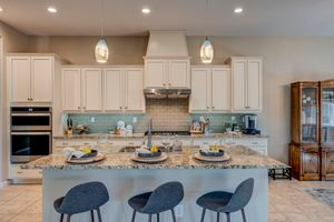 Bright kitchen featuring white cabinetry, granite island with bar seating, and pendant lighting.