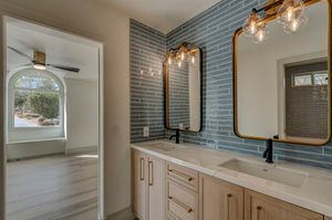 Modern bathroom with dual sinks, blue subway tile backsplash, gold-framed mirrors, and pendant lighting.