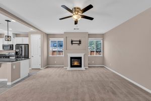 Spacious living room with ceiling fan, fireplace, neutral carpet, and open view to kitchen area.