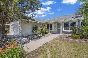 Single-story ranch home with attached garage, manicured landscaping, tall trees, and welcoming front walkway on sunny day.