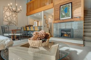 Rustic living room with high ceilings, stone fireplace, wood paneling, chandelier, and glass coffee table.