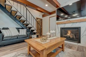 Inviting living room featuring marble fireplace, wood beam ceiling, leather sofa, and modern staircase.