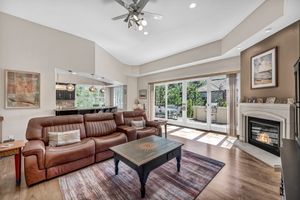 Spacious living room with vaulted ceilings, brown leather sectional sofa, hardwood floors, ceiling fan, and a cozy fireplace.