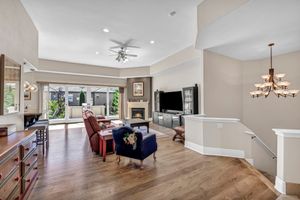 Elegant living room featuring hardwood floors, tray ceiling, gas fireplace, ceiling fan, and large windows with natural light.