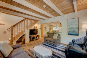 Rustic living room with wood beam ceiling, staircase, hardwood floors, and comfortable gray sofas.
