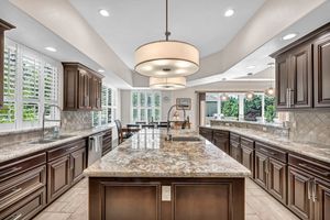 Gourmet kitchen with dark wood cabinets, granite island, pendant lighting, tile backsplash, and abundant natural light.