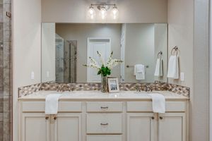 Master bathroom double vanity with mosaic tile backsplash, large mirror, and white cabinetry.
