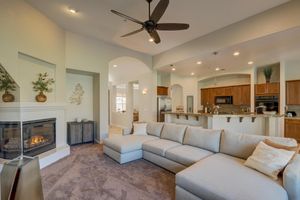 Bright living room with large sectional sofa, gas fireplace, ceiling fan, and open kitchen view.