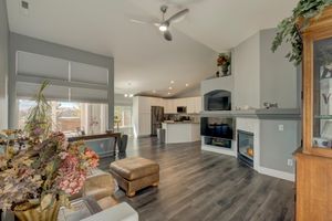 Open-concept living room with dark hardwood floors, vaulted ceiling, ceiling fan, and modern fireplace leading to kitchen.
