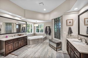 Luxurious master bathroom with double vanities, soaking tub, glass shower, dark wood cabinets, and large windows.