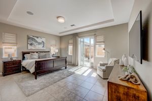 Spacious master bedroom with tray ceiling, patio access, sitting area, and wall-mounted TV.