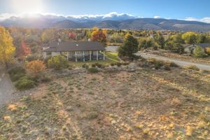 Aerial view of a ranch home surrounded by autumn foliage with snow-capped mountains in the background.