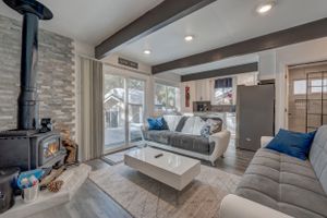 Modern cabin living room with gray sofas, wood beam ceiling, black wood stove, and sliding glass door.