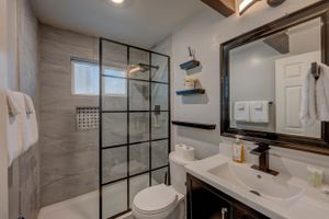 Contemporary bathroom with black-framed glass shower, gray tile walls, white vanity, and modern fixtures.