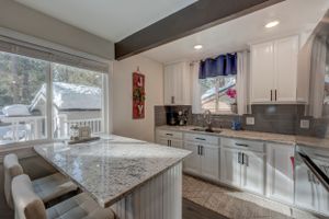 Bright kitchen with white cabinets, granite countertop island, gray backsplash, and snowy window view.