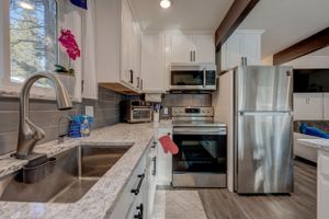 Modern kitchen with white cabinets, granite counters, stainless steel appliances, and gray tile backsplash.