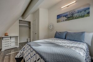 Cozy sloped-ceiling bedroom with queen bed, blue accents, barn door closet, and coastal wall art.