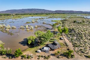 Aerial view of rural property surrounded by flooded wetlands, desert landscape, and mountain views.