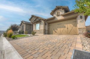 Elegant single-story home with stone accents, decorative brick paver driveway, and two-car garage.