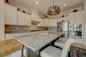 Modern white kitchen with granite island, stainless steel appliances, tile backsplash, and pendant lighting.