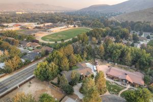 Aerial view of a green ranch-style property nestled among mature trees near scenic mountains.