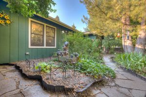 Charming green exterior home with a lush garden pathway featuring sunflowers and decorative plants.
