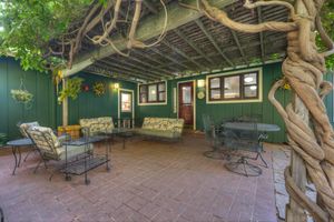 Cozy brick patio with wisteria pergola, wrought iron furniture, and green wood-paneled walls.