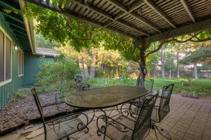Outdoor brick patio with wrought iron dining set under a lush green wisteria pergola.