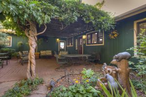 Rustic brick patio with wisteria-covered pergola, wrought iron furniture, and decorative garden sculptures.