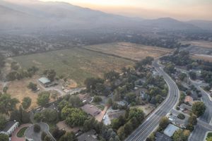 Aerial view of a suburban community with open fields, tree-lined roads, and mountain backdrop at dusk.