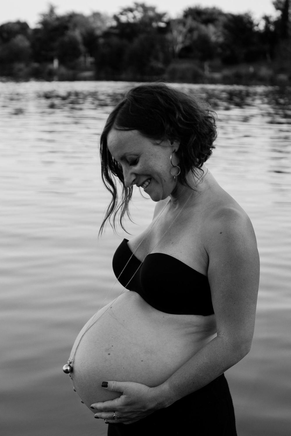 A black and white maternity photo taken by a serene lake.