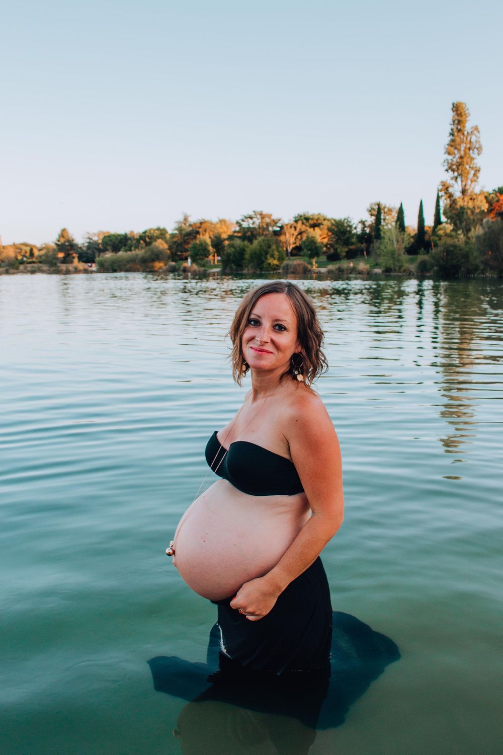 An expectant figure stands in serene lake waters wearing a black swimsuit.