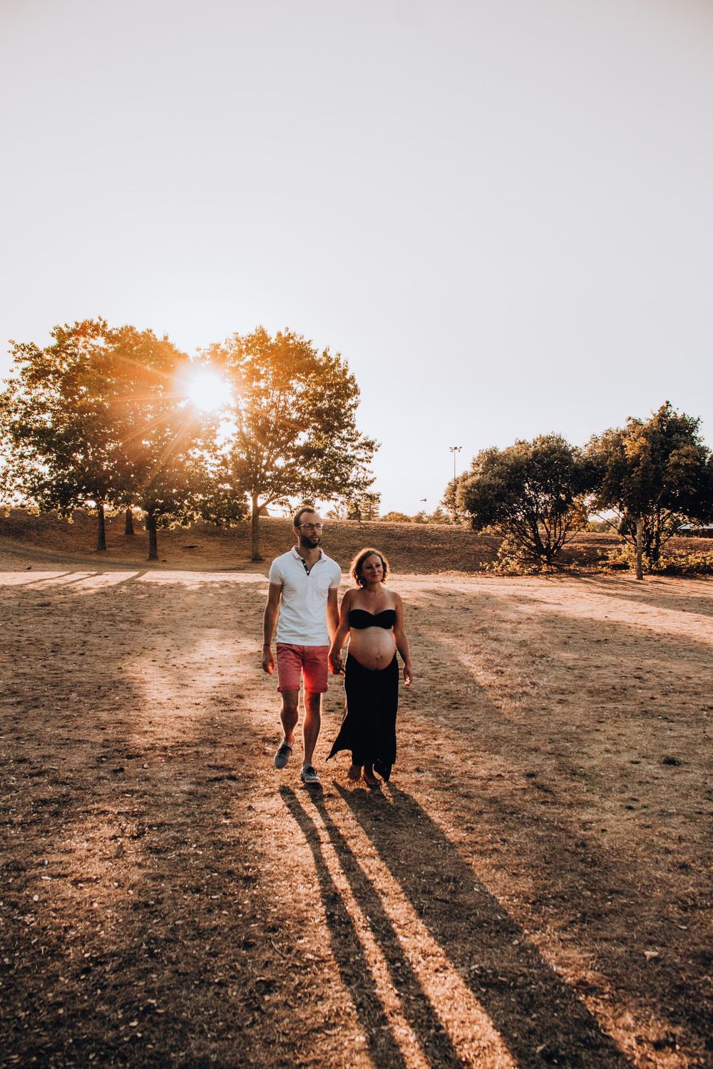 A couple walks hand in hand on a dusty trail during sunset.