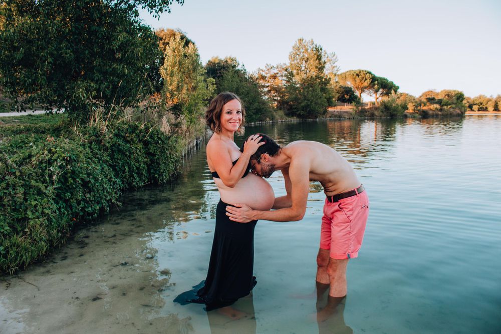 A couple shares a joyful moment during their maternity photoshoot at the water's edge.