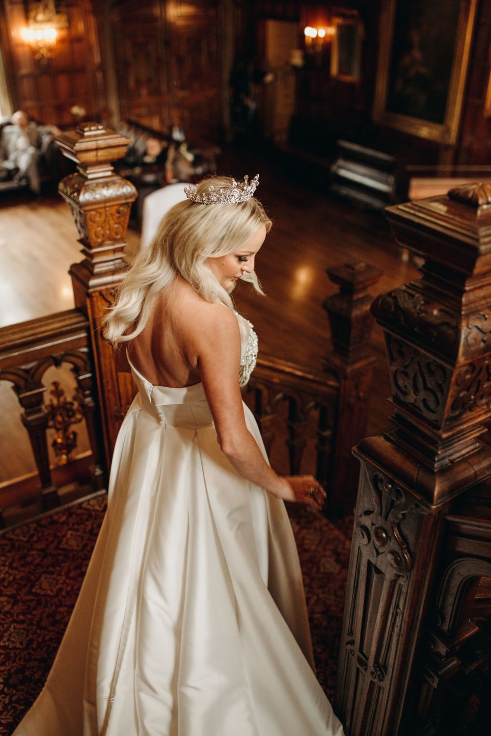 Elegant wedding dress photographed from behind on ornate wooden staircase.