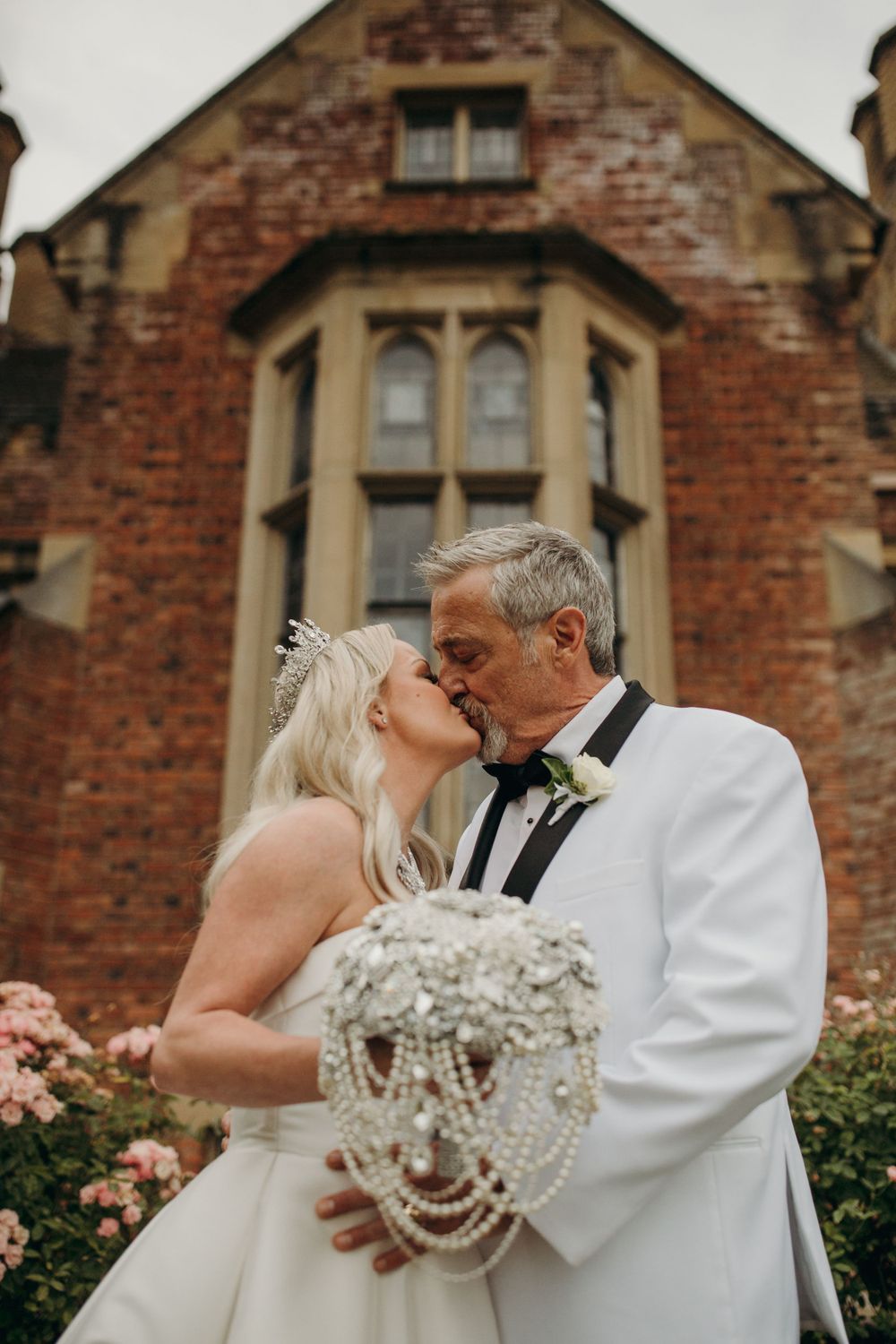 A romantic wedding portrait in front of a Gothic-style brick building with roses.