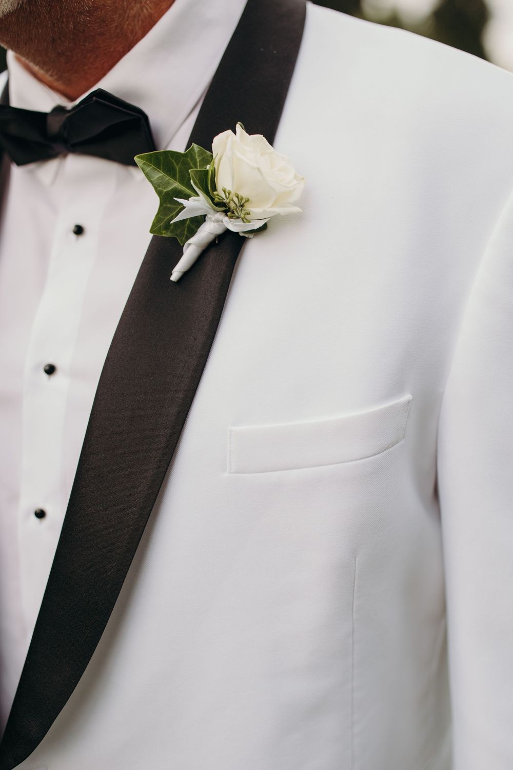 Close-up of a white boutonniere on a white tuxedo jacket with black lapels.