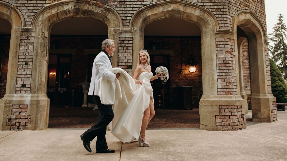 Wedding couple walking through stone archway entrance with dress billowing.