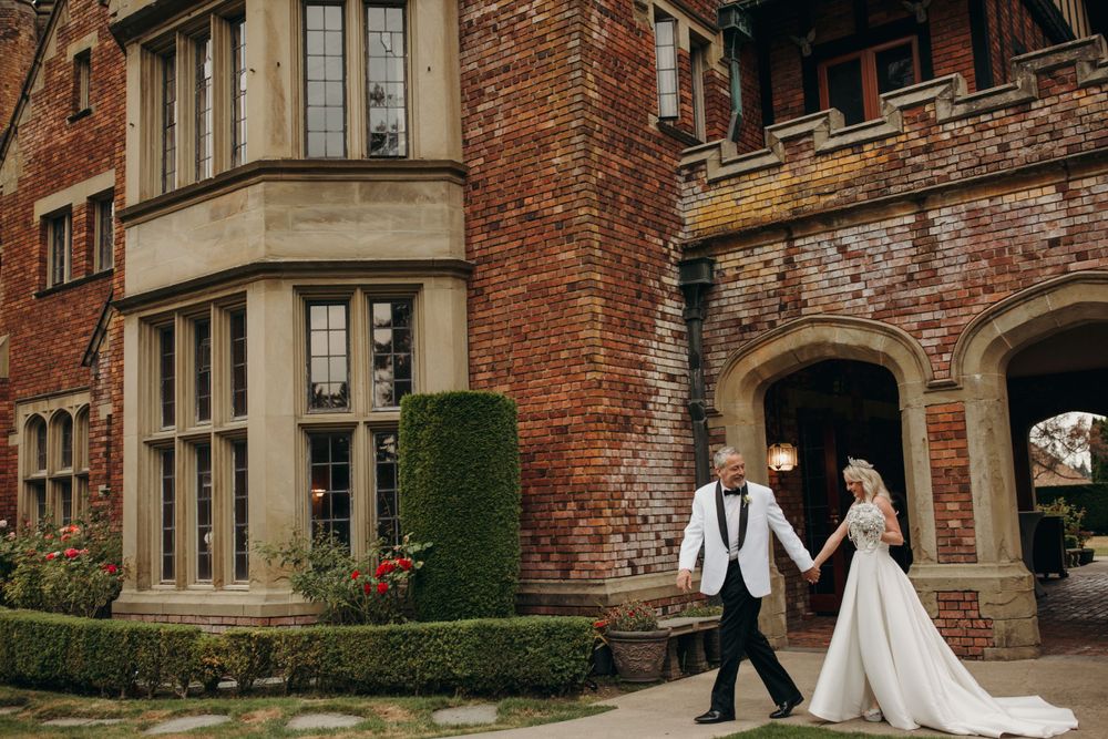 A wedding couple walking outside a grand historic red brick mansion with ornate architectural details.