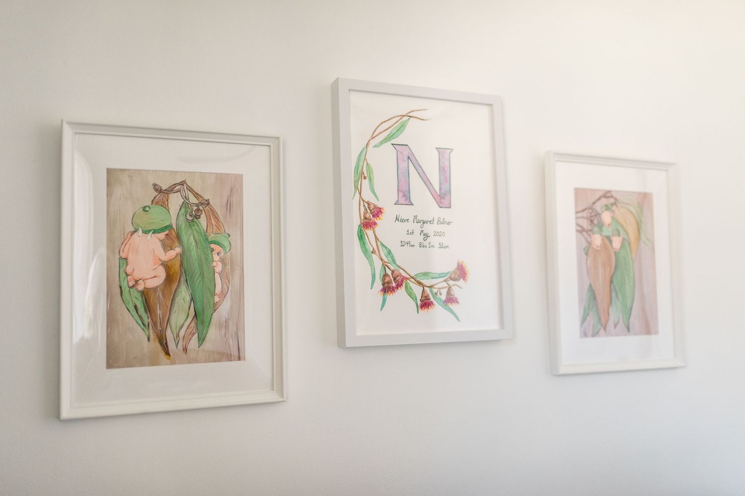 Three framed art prints featuring botanical illustrations and monogram design on white wall.
