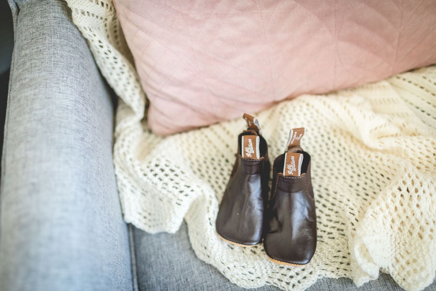 Two small brown leather baby shoes rest on a cream colored knit blanket.