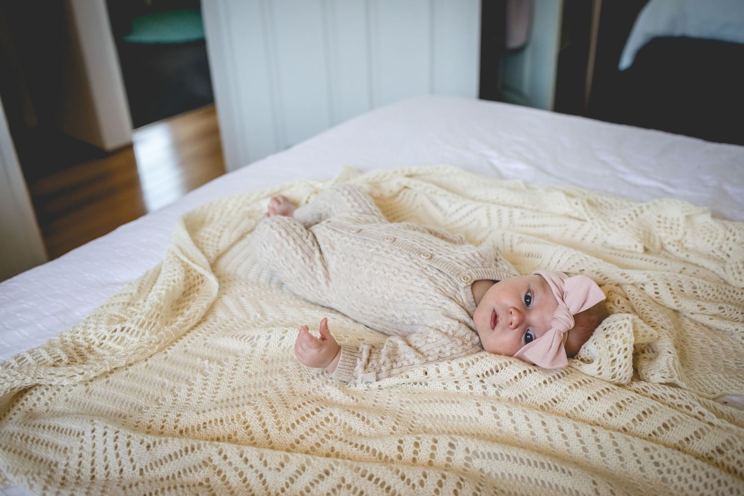 A cream colored knitted blanket arranged on a white surface in soft lighting.